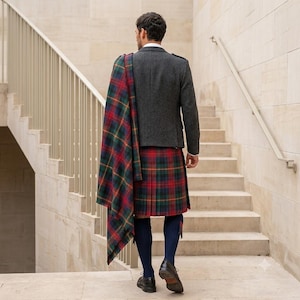 May include: A charcoal gray wool blazer worn with a traditional pleated kilt in a red, green, and blue tartan pattern. A matching tartan plaid is draped over the shoulder. The outfit includes navy blue knee-high socks and dark brown leather shoes.