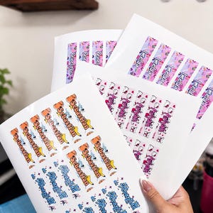 May include: Multiple sheets of rectangular adhesive labels featuring various names including Sebastian, Imelda, and Arivyah. The labels display colorful cartoon graphics, including Pikachu and Hello Kitty, with repeating text patterns on a white background.