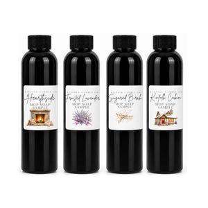 May include: Four black plastic bottles with black caps, each featuring a white label with the text Kinfolk Candle Co, Mop Soap Sample, and a unique illustration: a fireplace, lavender, birch branches, and a cabin in the snow.