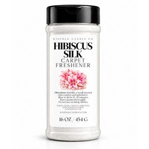 May include: A clear plastic shaker bottle with a black flip-top lid containing white powder. The label reads KINFOLK CANDLE CO HIBISCUS SILK CARPET FRESHENER, features a pink hibiscus flower illustration, and lists 16 OZ / 454 G.