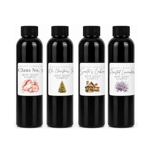May include: Four black plastic bottles with black screw caps, each featuring a white label with the text Kinfolk Candle Co, Mop Soap Sample, and unique scent names: Claus No. 5, Oh Christmas Tree, Santa's Cabin, and Frosted Lavender with illustrations.