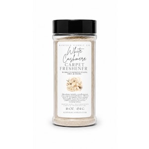 Könnte beinhalten: Eine durchsichtige Kunststoff-Streudose mit schwarzem Deckel, gefüllt mit beigem Teppichreinigungspulver. Das Etikett trägt die Aufschrift Kinfolk Candle Co White Cashmere Carpet Freshener, 16 oz / 454 g, inklusive Anleitung, Inhaltsstoffen und Blumenmotiv.