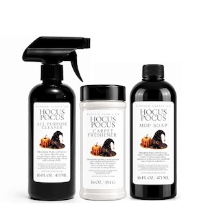 Może przedstawiać: Trzy czarne butelki i pojemnik z etykietą Hocus Pocus. Po lewej spray do czyszczenia powierzchni 473 ml, w środku odświeżacz do dywanów 454 g, a po prawej mydło do mycia podłóg 473 ml, wszystkie z pasującymi do siebie etykietami graficznymi.