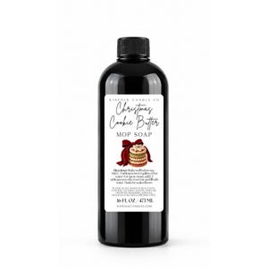 May include: A black plastic bottle containing 16 fl. oz. of Christmas Cookie Butter mop soap. The white label features the text Kinfolk Candle Co, Christmas Cookie Butter, Mop Soap, directions, ingredients, and an illustration of stacked cookies.