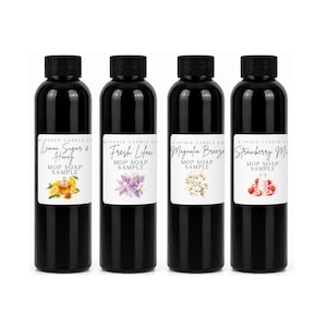 May include: Four black plastic bottles with black screw caps, each featuring a white label with the text Kinfolk Candle Co, Mop Soap Sample, and specific scent names: Lemon Sugar & Honey, Fresh Lilac, Magnolia Breeze, and Strawberry Milk.