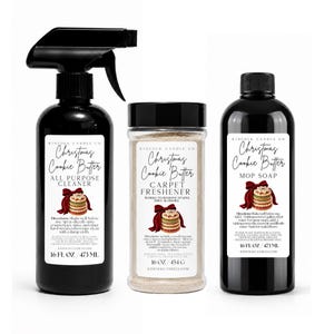 Może przedstawiać: Trzy czarne pojemniki z etykietą Kinfolk Candle Co. Christmas Cookie Butter. Butelka ze sprayem do czyszczenia powierzchni, pojemnik z odświeżaczem do dywanów oraz butelka mydła do podłóg z grafiką ciastek i czerwoną kokardą.