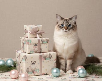 May include: A Ragdoll cat with blue eyes sits near wrapped gifts and Christmas ornaments. The gifts are wrapped in patterned paper with a cat design and tied with a ribbon. Pink and blue ornaments and greenery are scattered around.