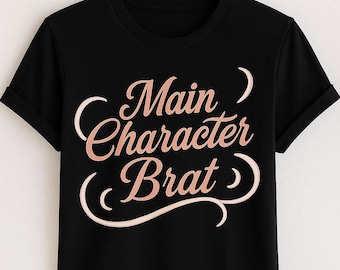 May include: Black t-shirt with the phrase "Main Character Brat" in a cursive, rose-gold font. The text is centered on the shirt, which is hanging on a wooden hanger. The sleeves are cuffed.
