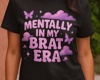 May include: Black t-shirt with the phrase "MENTALLY IN MY BRAT ERA" in pink, with butterfly and cloud graphics. The shirt is a crew neck style.