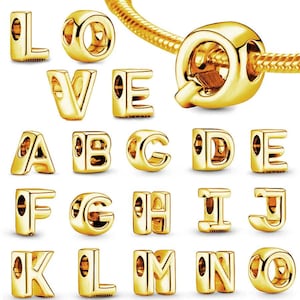 Op de afbeelding: Een verzameling goudkleurige alfabetbedels, waaronder de letters L, O, V, E, A, B, C, D, E, F, G, H, I, J, K, L, M en N. De bedels zijn ontworpen om te worden gebruikt met een armband of ketting. De letters zijn in een schreefloze lettertype.