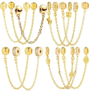 Può includere: Braccialetti con ciondoli color oro con varie perline decorative e clip di sicurezza a catena. I ciondoli includono disegni a cuore, fiori e rotondi, alcuni con accenti di cristallo trasparente. I braccialetti sono esposti su sfondo bianco.