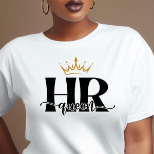 May include: A white short-sleeved t-shirt featuring a graphic print on the chest. The design includes large black letters reading HR, a gold crown icon positioned above the letters, and the word queen in black cursive script below.