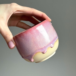 Pode incluir: Uma tigela de cerâmica artesanal com acabamento brilhante. A tigela apresenta um gradiente de cores, passando do rosa intenso no topo para o amarelo claro na base. A cobertura rosa escorre pela lateral, criando uma textura única.