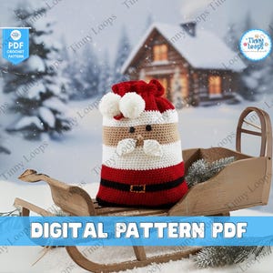 May include: A crocheted Santa Claus bag with a red hat and white pom-poms sits on a wooden sled. The bag has a red body, a white beard, and a tan face. The words "DIGITAL PATTERN PDF" are displayed on the bottom of the image.