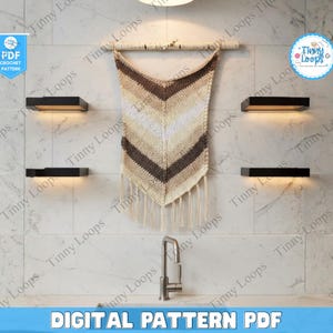 May include: A crochet wall hanging with a chevron pattern in shades of brown, beige, and cream, suspended from a birch branch. The image also shows the text "DIGITAL PATTERN PDF" and the logo "Tinny Loops".