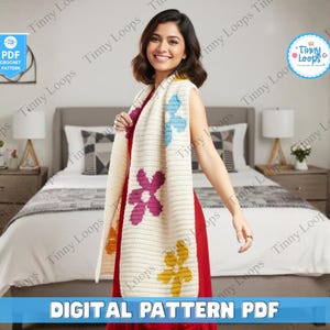 Könnte beinhalten: Ein cremefarbener Häkelschal mit großen, farbenfrohen Blumenmustern in Lila, Blau und Gelb. Der Schal ist über einer Person drapiert. Das Bild enthält auch den Text "DIGITAL PATTERN PDF" und das Logo von "Tinny Loops".