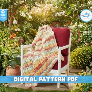 May include: A white wooden chair with a red cushion is draped with a colorful, patterned blanket. The blanket features a mix of yellow, orange, and blue hues. The image is set in a garden with lush greenery and flowers. Text on the image reads "DIGITAL PATTERN PDF".