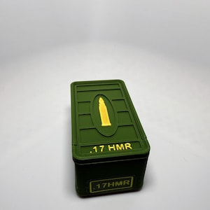May include: A green rectangular box with a gold bullet graphic on the lid. The text ".17 HMR" is printed in yellow on the lid and the side of the box. The box is likely for ammunition storage.