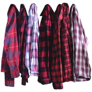 May include: Seven plaid flannel shirts in various shades of red, black, and white. The shirts are hanging on a white background.