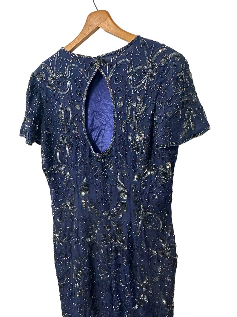 May include: A navy blue sequined dress with a keyhole back. The dress is covered in a floral pattern and has short sleeves.