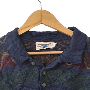 May include: A blue and brown patterned knit sweater with a collared neckline and a button closure. The sweater has a label that reads "Pierre Cardin".