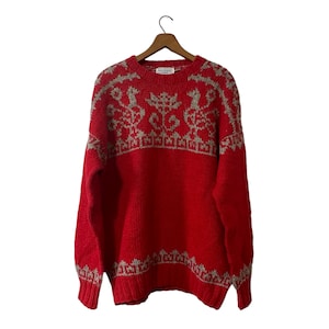 May include: Red knitted jumper with a white and grey geometric pattern. The jumper has long sleeves and a crew neck.