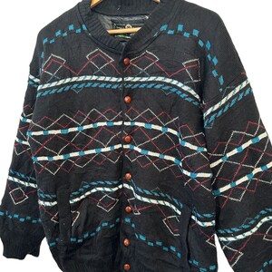 May include: A black knitted cardigan with a geometric pattern in blue, white, and red. The cardigan has a button-up front and two pockets.