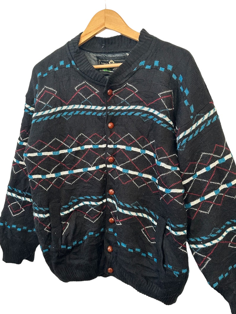 May include: A black knitted cardigan with a geometric pattern in blue, white, and red. The cardigan has a button-up front and two pockets.