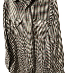 May include: A long-sleeved plaid shirt in a brown, green, red, and black checkered pattern. The shirt has a button-up front and two chest pockets. The label on the shirt reads "The Bearded Bee".