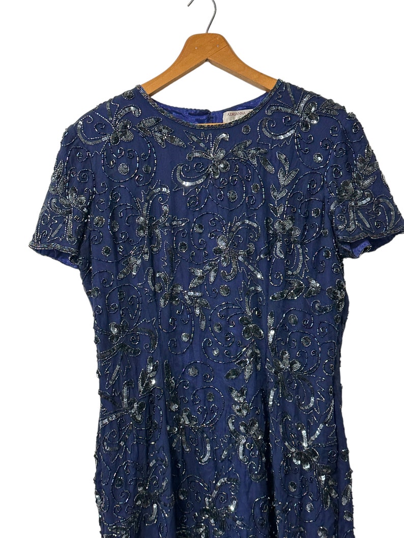 May include: A navy blue sequined dress with a floral pattern. The dress has short sleeves and a round neckline. The dress is made of a soft, flowing fabric and is perfect for a special occasion.