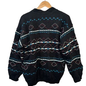 May include: Black sweater with a geometric pattern in shades of blue, red, and white. The sweater has a crew neck and long sleeves.