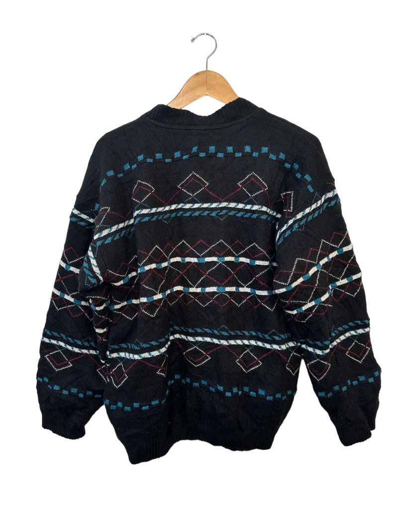 May include: Black sweater with a geometric pattern in shades of blue, red, and white. The sweater has a crew neck and long sleeves.