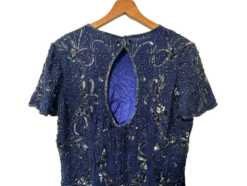 May include: A navy blue sequined dress with a low back and short sleeves. The dress is covered in intricate floral patterns and sequins.