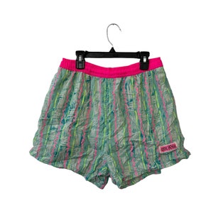 May include: Green and pink patterned swim shorts with a pink elastic waistband and a pink "Ocean Pacific" logo.