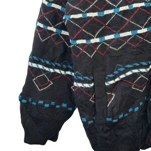 May include: Black knitted cardigan with a geometric pattern in red, white, and blue. The cardigan has a pocket on the left side.