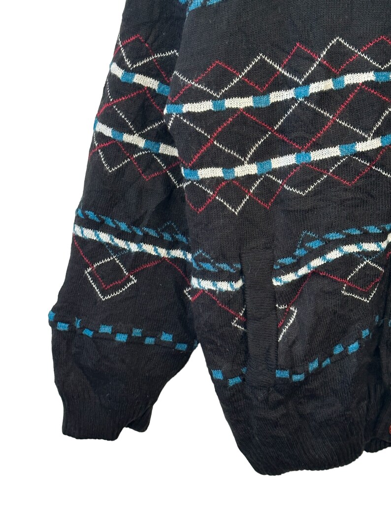 May include: Black knitted cardigan with a geometric pattern in red, white, and blue. The cardigan has a pocket on the left side.