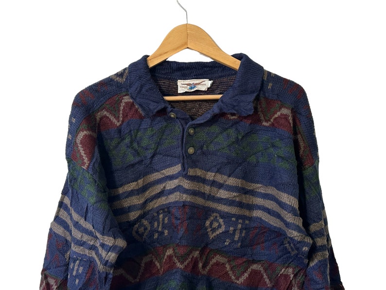 May include: A blue, green, and red patterned sweater with a collared neckline and button closure. The sweater has a striped pattern and a geometric design.