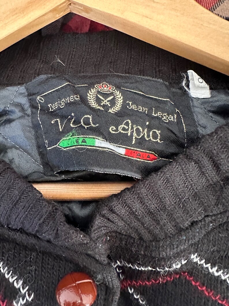 May include: Black and red plaid sweater with a brown button and a label that reads "Designed Via eapia Jean Legal!"