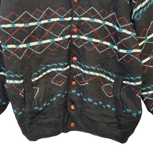 May include: A black cardigan sweater with a diamond pattern in shades of blue, white, and red. The sweater has a button-up front and two pockets.