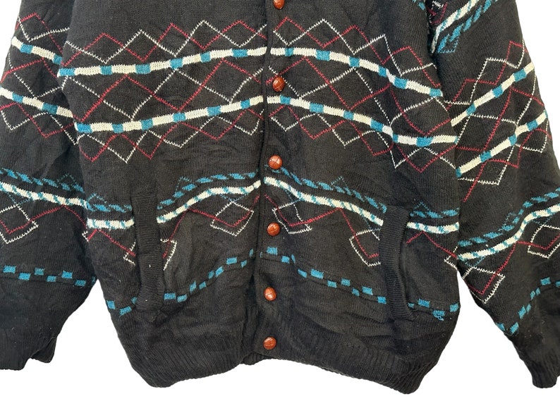 May include: A black cardigan sweater with a diamond pattern in shades of blue, white, and red. The sweater has a button-up front and two pockets.