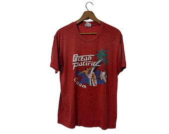May include: Red t-shirt with a faded graphic of a surfer on a wave with the text "Ocean Pacific Guam".