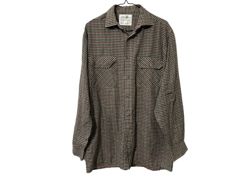 May include: A long-sleeved plaid shirt with a button-up front and two flap pockets. The shirt is in a brown, black, red, and white plaid pattern. The shirt has a label that reads "John Henry  Co."