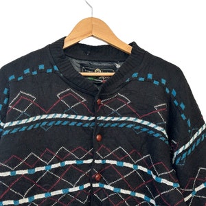 May include: Black knitted cardigan with a geometric pattern in blue, white, and red. The cardigan has a button closure and a v-neck.