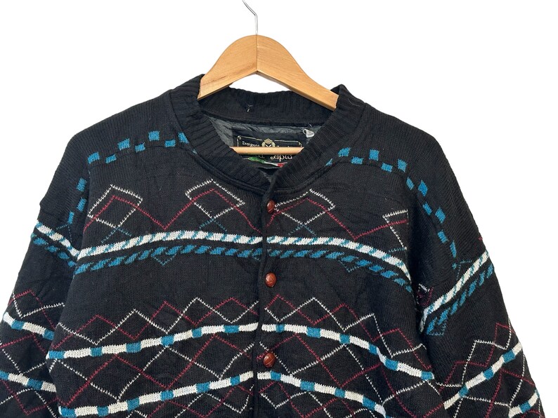 May include: Black knitted cardigan with a geometric pattern in blue, white, and red. The cardigan has a button closure and a v-neck.