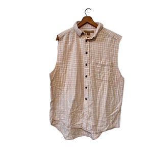 May include: A sleeveless button-down shirt with a white and light brown gingham pattern. The shirt has a collared neckline and a single chest pocket.