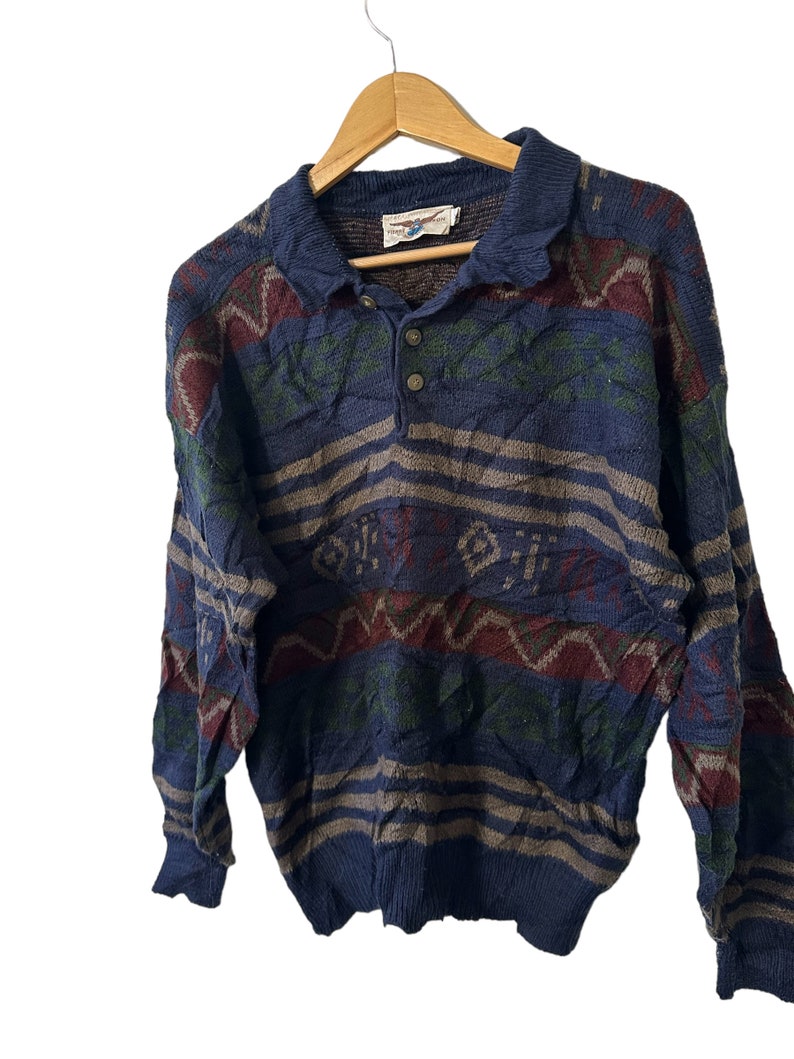 May include: A blue, long-sleeved sweater with a multi-colored geometric pattern. The sweater has a button-up collar and a single button closure.
