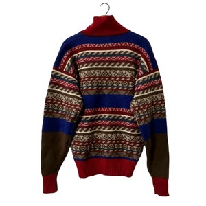 K&ouml;nnte beinhalten: Ein Pullover mit hohem Kragen in einem Muster aus Blau, Rot, Braun und Wei&szlig;.
