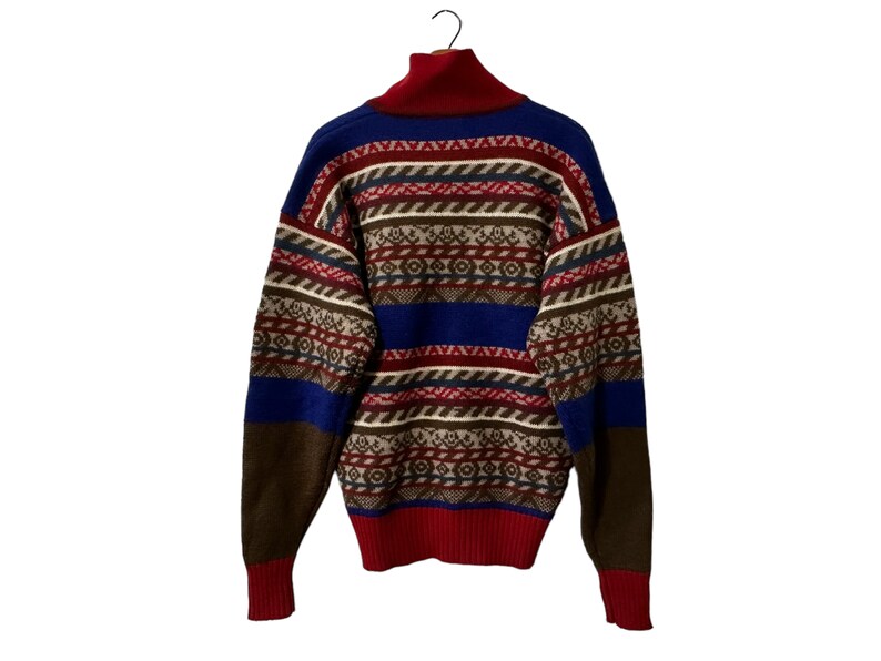K&ouml;nnte beinhalten: Ein Pullover mit hohem Kragen in einem Muster aus Blau, Rot, Braun und Wei&szlig;.