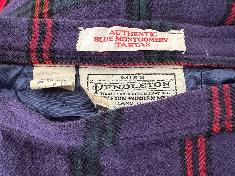 Op de afbeelding: Een paarse, zwarte en rode geruite rok met een wit label waarop "Miss Pendleton" en "Authentic Blue Montgomery Tartan" staat.