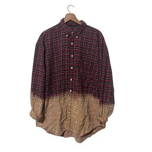 May include: A red and black checked flannel shirt with a faded, ombre effect transitioning to a tan colour at the bottom.